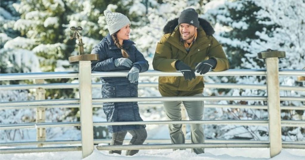 man and woman wearing columbia winter jackets on a bridge in the snow