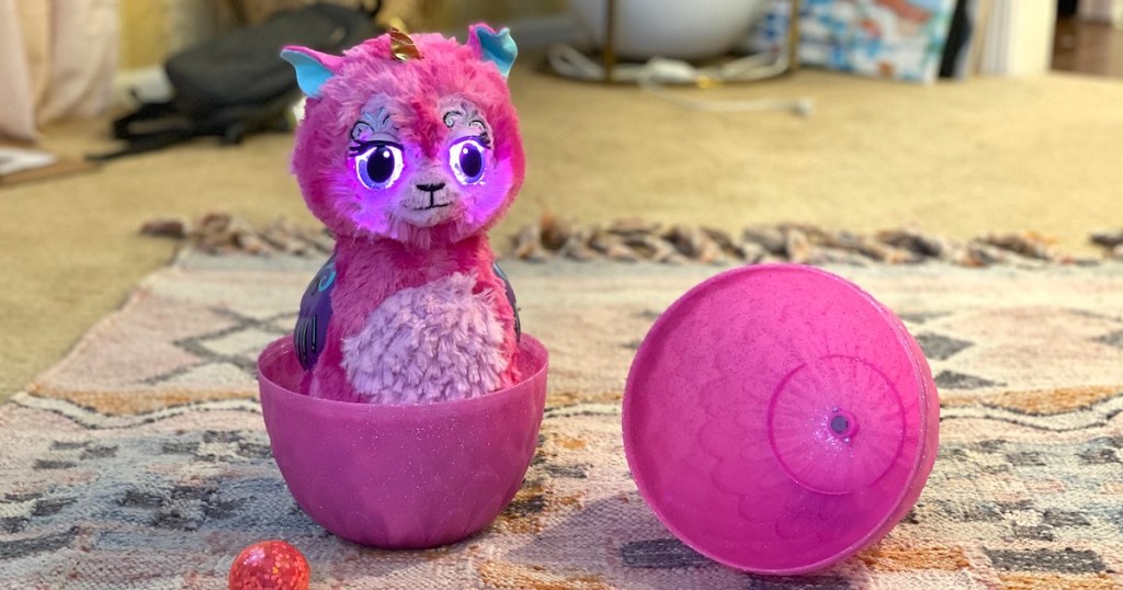 pink hatchimal toy that grows sitting on rug 