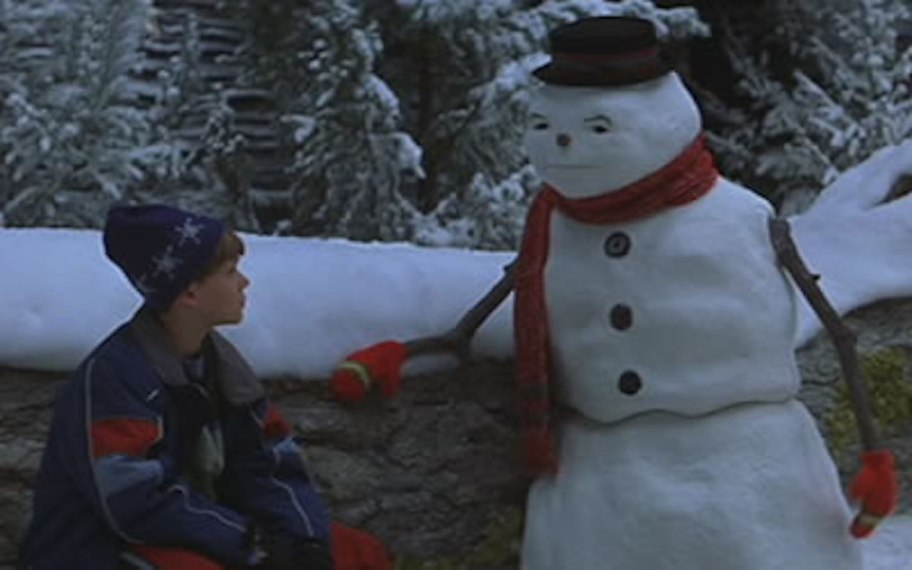 boy sitting outside with snowman 