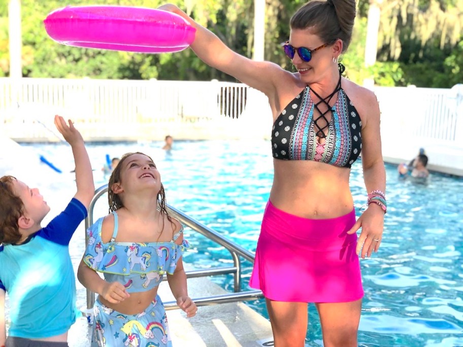 woman wearing pink skirt playing with pool float and two kids at pool