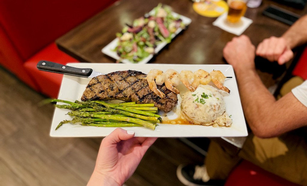 hand holding a steak dinner on plate