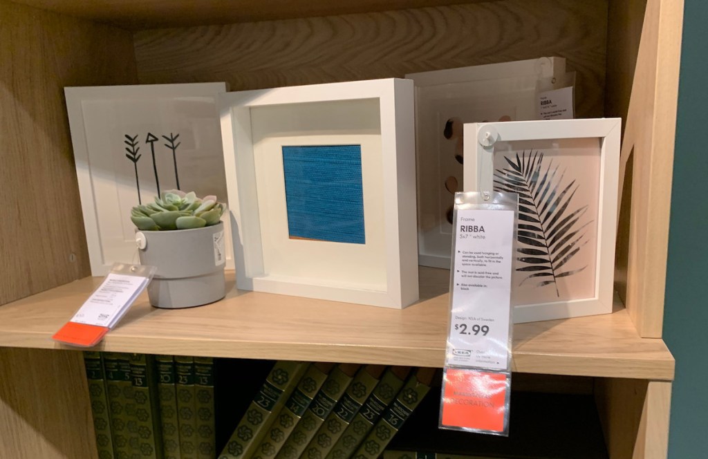 various sizes of square white picture frames sitting on wood bookshelf 