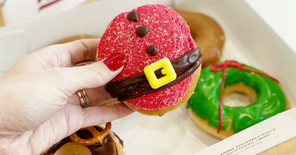 lady holding a Santa Doughnut Krispy Kreme with other Christmas doughnuts in the backround