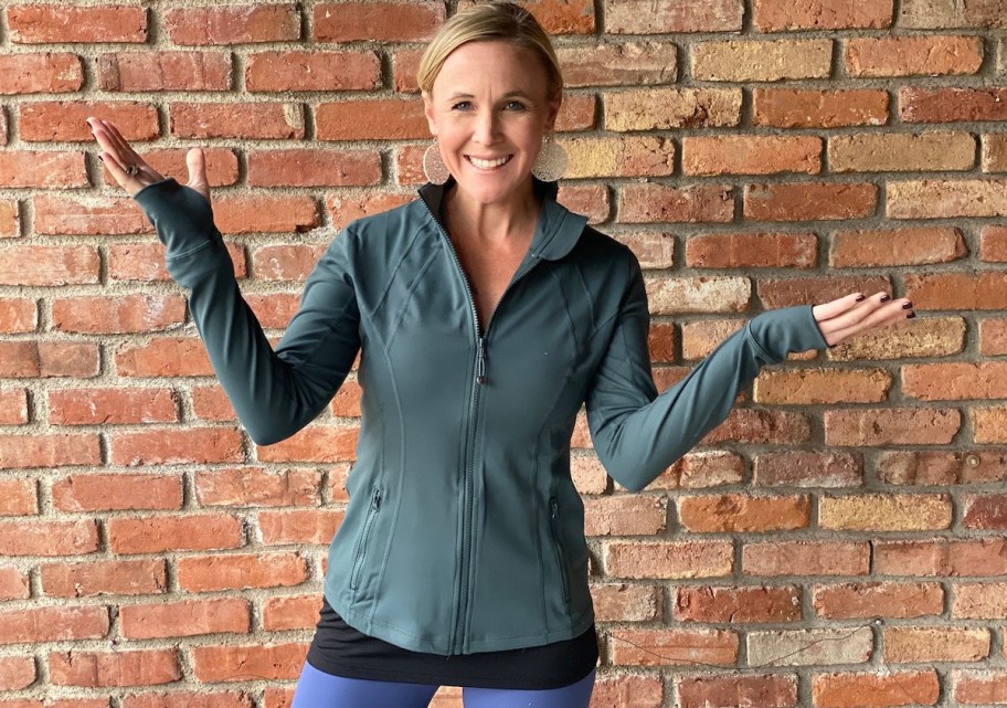 woman wearing green tight fitted jacket standing in front of brick wall