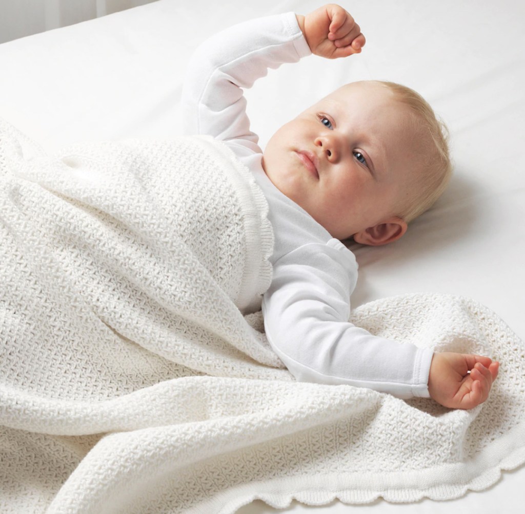 Baby laying on bed with white blanket on top