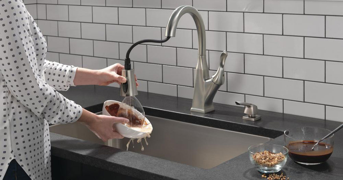 woman standing by her sink using the Delta Everly Single-Handle Pull-Down Sprayer Kitchen Faucet with ShieldSpray Technology in SpotShield Stainless