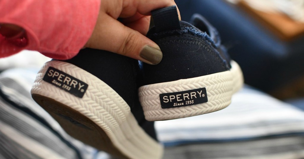 holding pair of blue Sperry shoes 