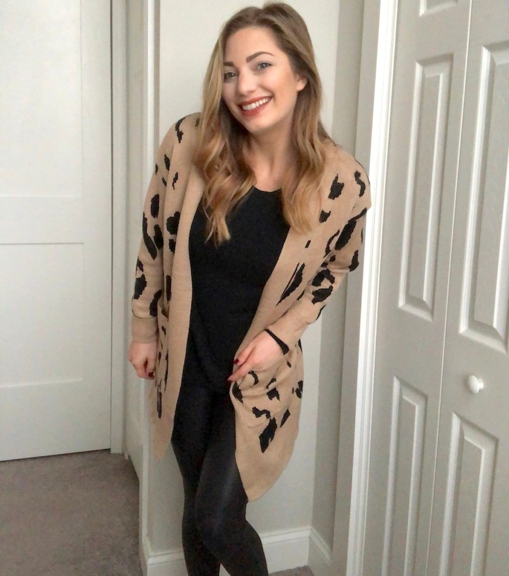 woman smiling wearing beige and black leopard cardigan and black leggings and shirt