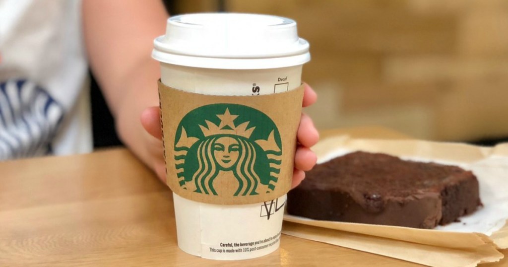 hand holding cup of coffee next to chocolate bread at table