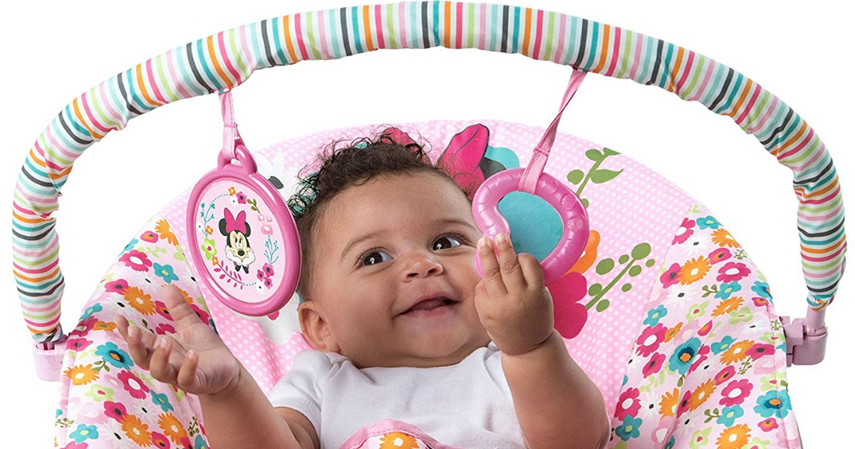 baby in pink seat batting at toys on bar above her head