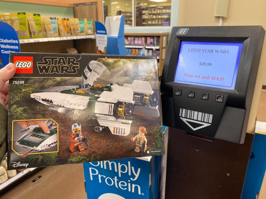 Hand holding Lego Star Wars Ship next to Kroger scanner