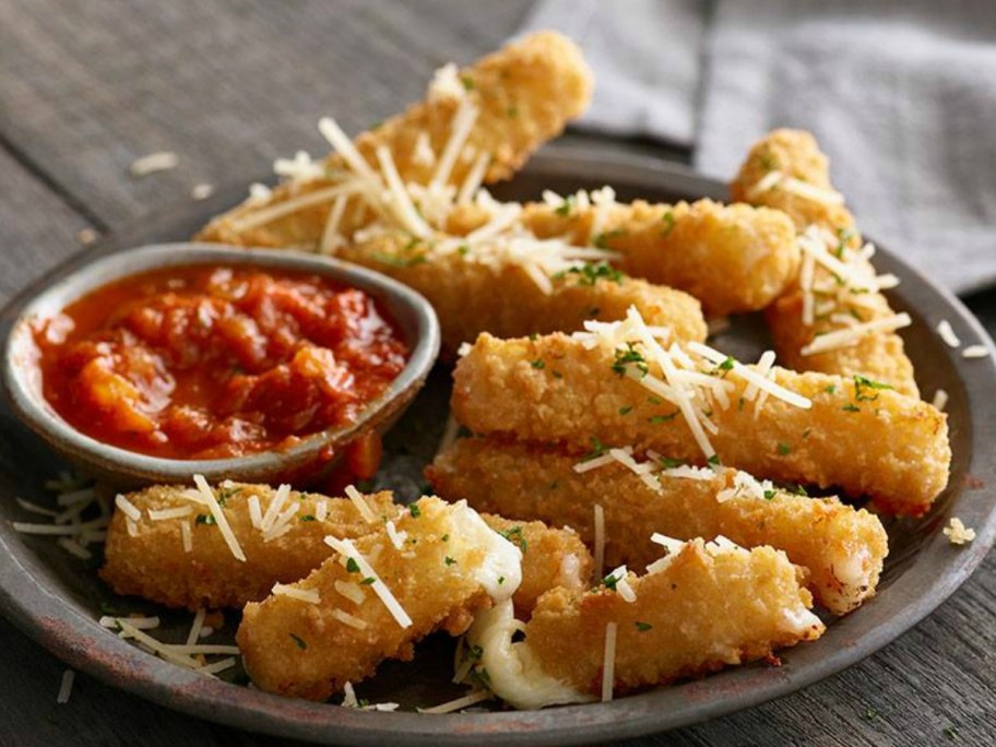 Large plate full of fried mozzarella sticks with a dipping container of marinara sauce