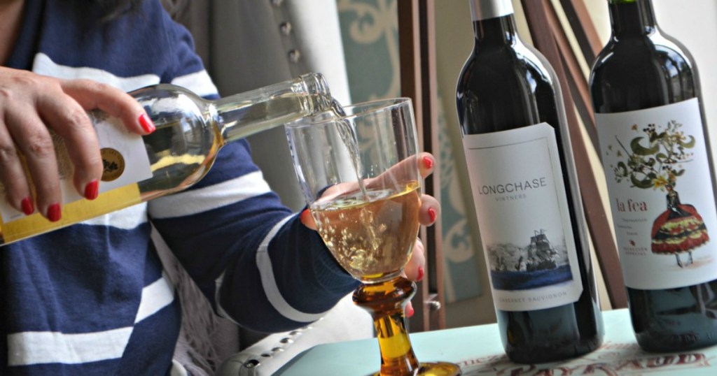 woman pouring wine into a glass next to two other wine bottles