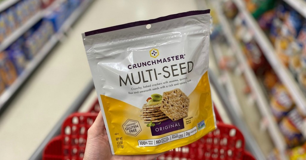 hand holding bag of crackers in front of grocery cart in store