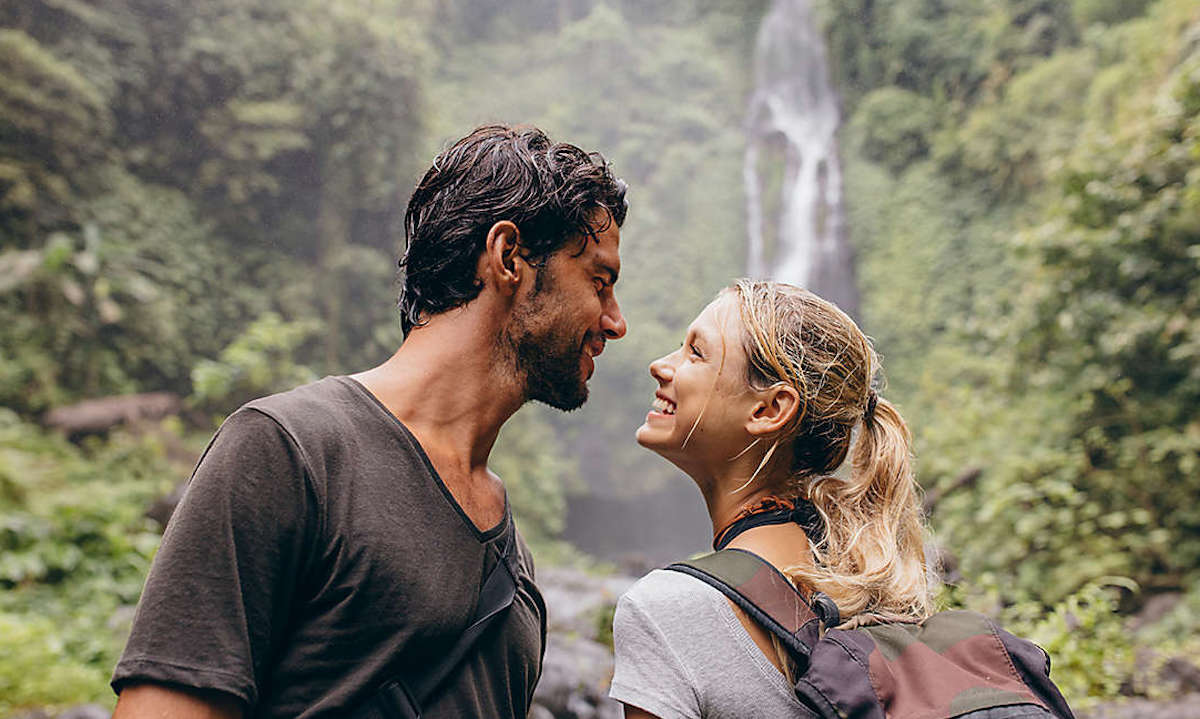 happy couple smiling at each other standing outside in front of waterfall