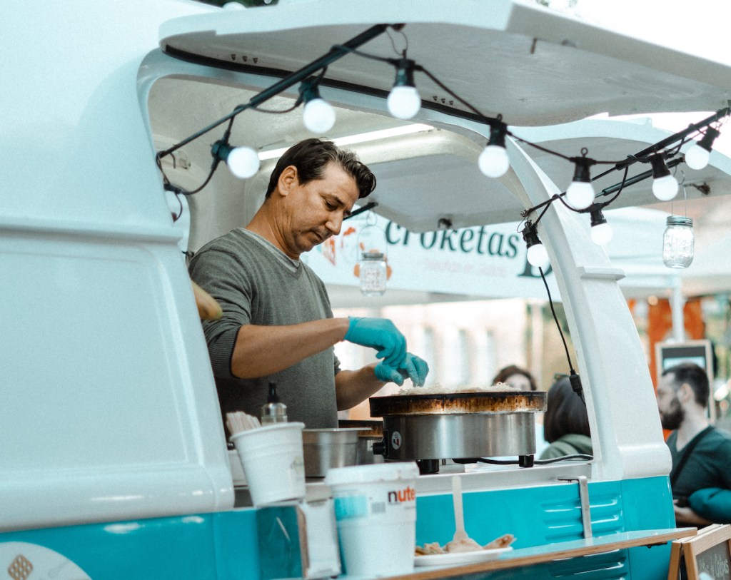 man serving food from food truck with string lights