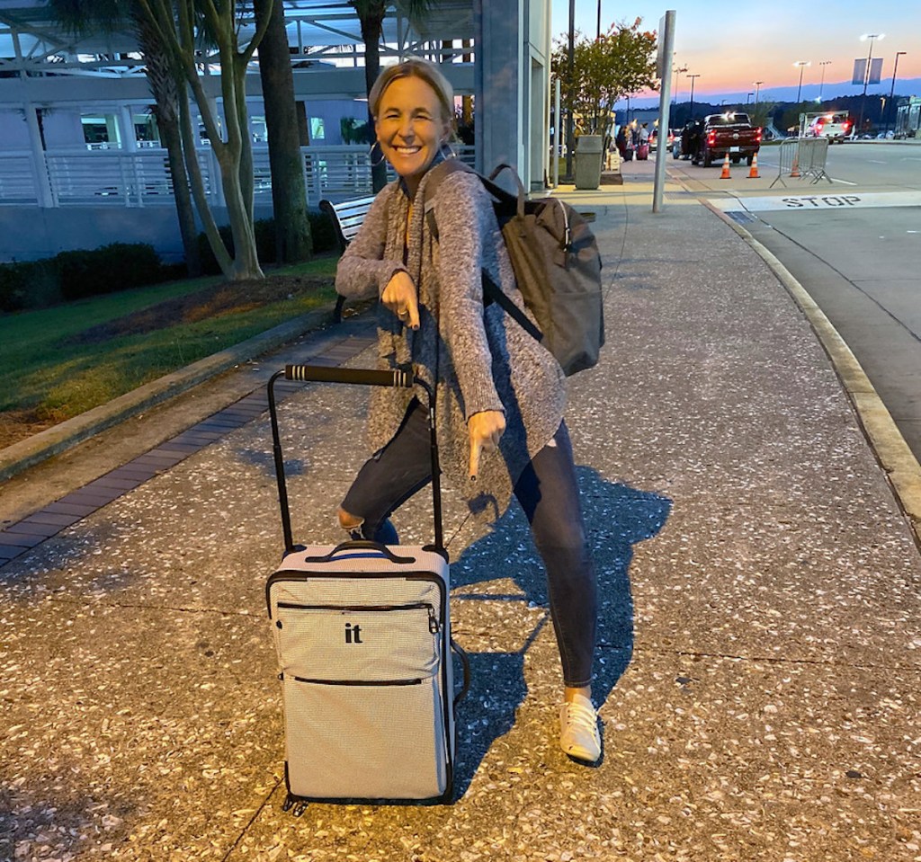 woman holding carry on luggage and bookbag on sidewalk