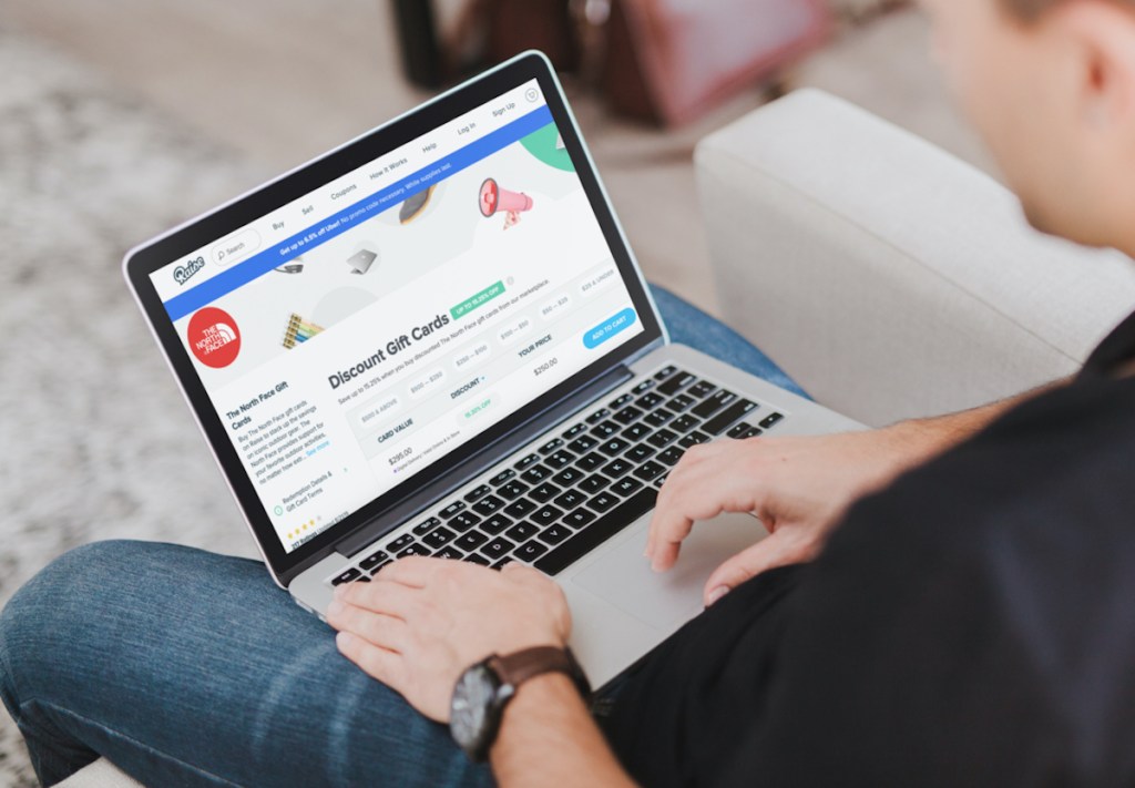 man sitting on couch with laptop on lap with raise discounted gift cards on screen