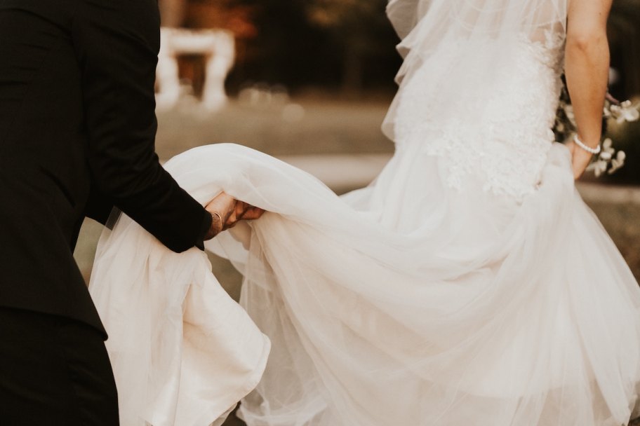 person in black holding back of brides wedding dress while walking wedding ideas on a budget