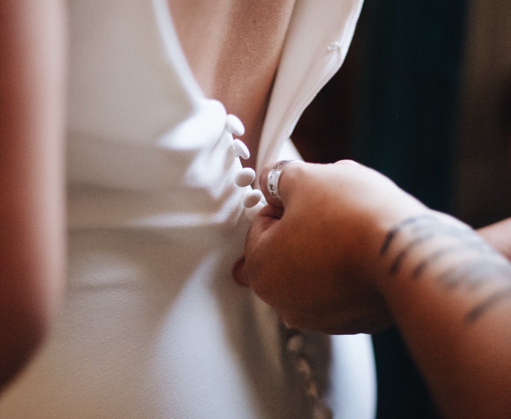 hands zipping up back of crepe white wedding dress with buttons on back