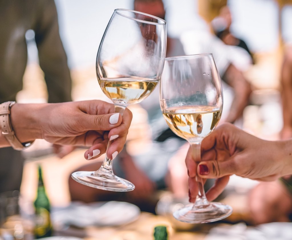 two hands holding white wine glasses doing a cheers