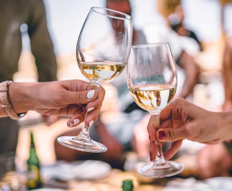 two hands holding white wine glasses doing a cheers wedding ideas on a budget