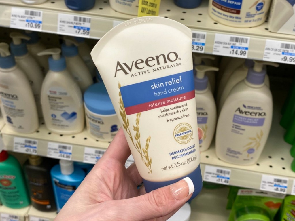 Hand holding a tube of Aveeno brand hand cream near in-store display