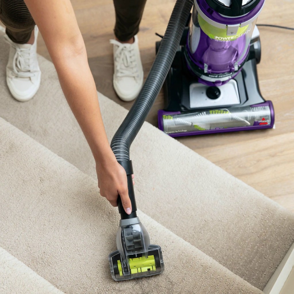 Woman using a vacuum attachment to clean carpeted stairs