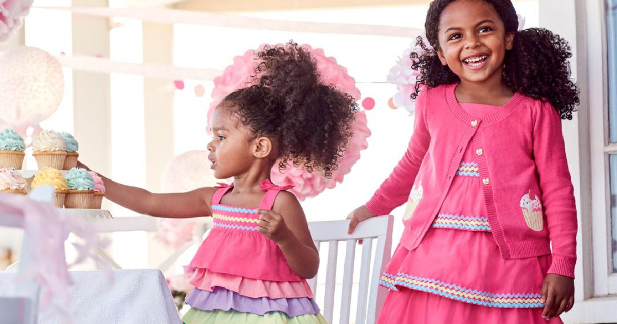 two young girls wearing gymboree hello cupcake outfits outside with balloons