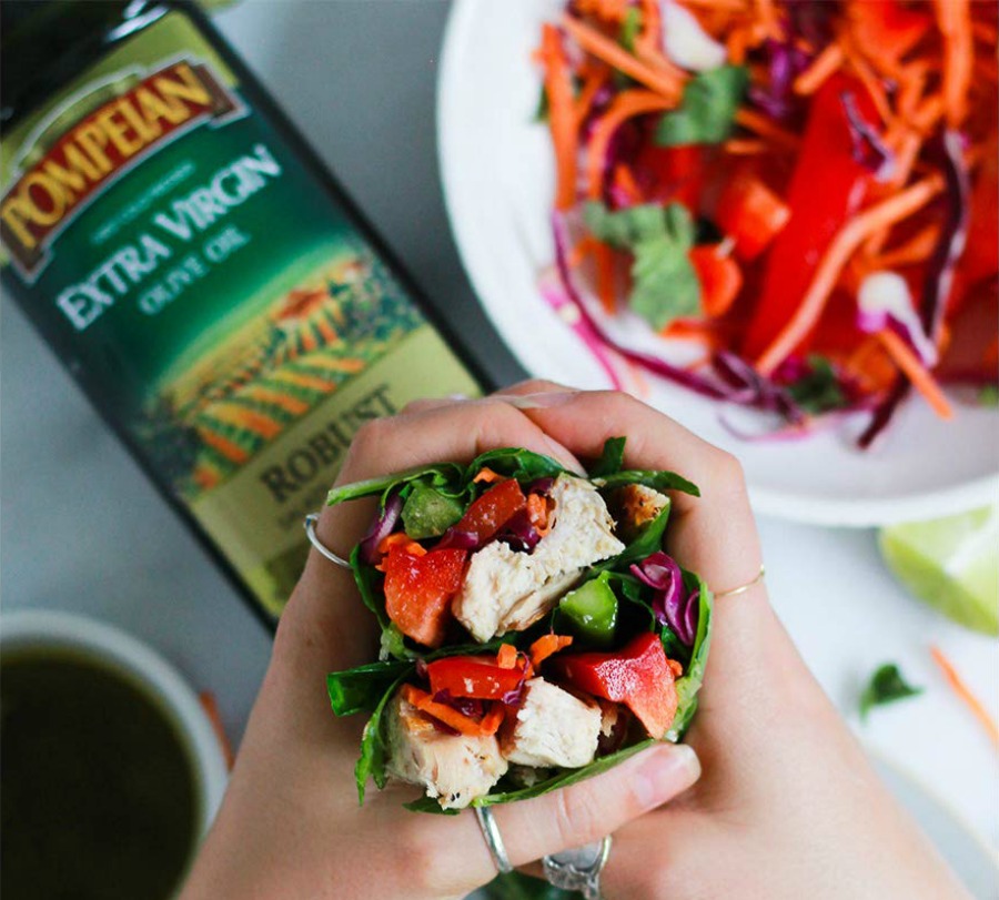 Hand holding veggies above Pompeian Extra Virgin Olive Oil