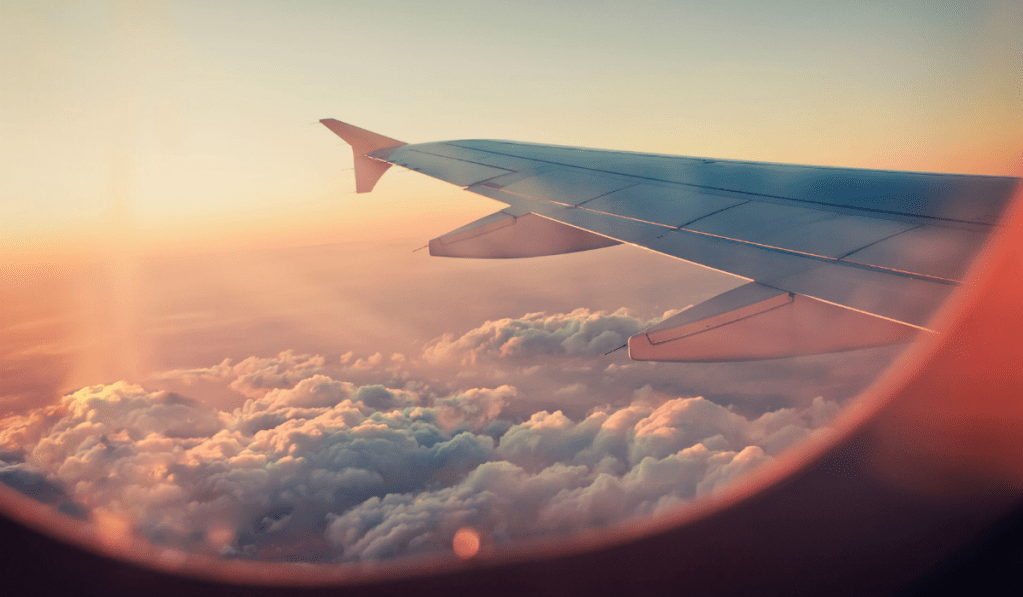 View of plane wing in the sky in the clouds out the window