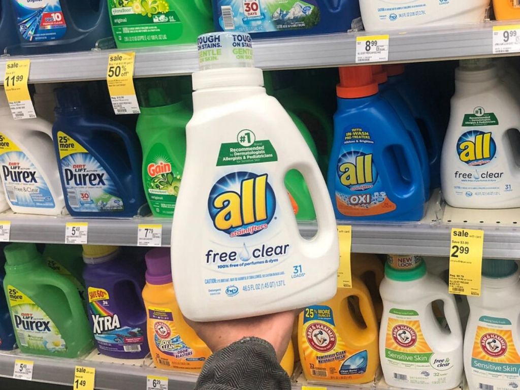 human hand displaying bottle of laundry detergent in front of store shelf