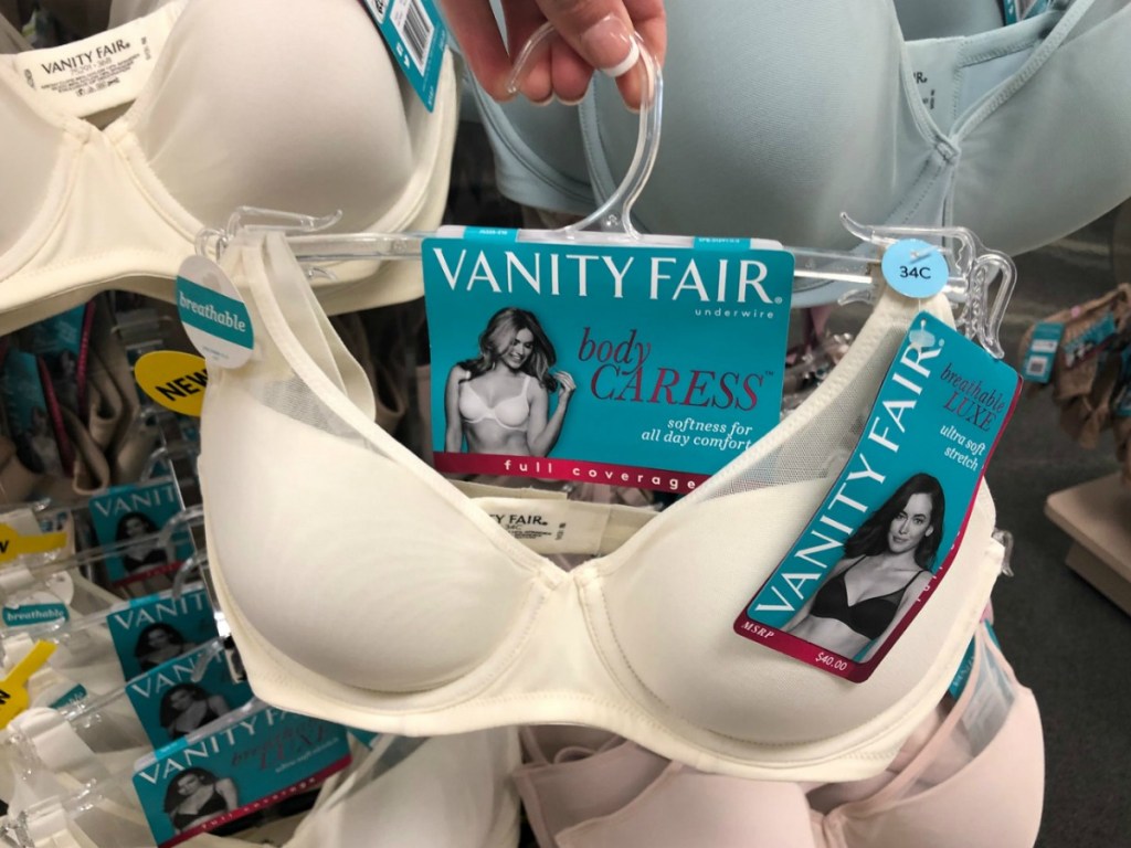 Hand holding up a white bra on a hanger near in-store intimates display