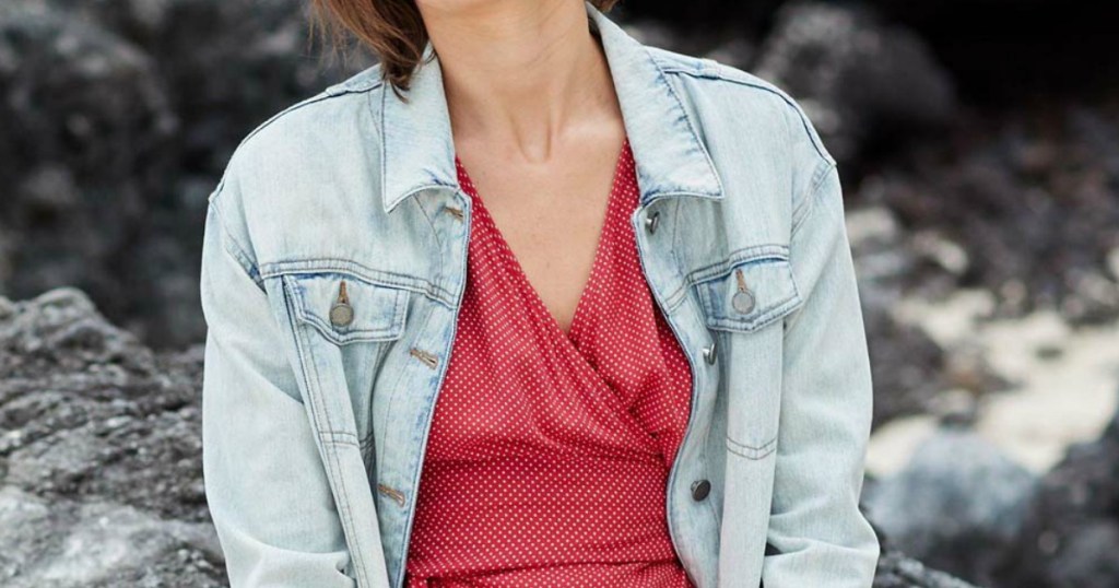 Woman sitting on a rocky terrain outdoors, wearing a bleached denim jacket and red dress