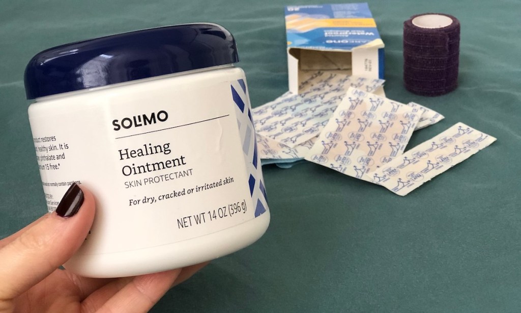 hand holding container of healing ointment with bandaids in background