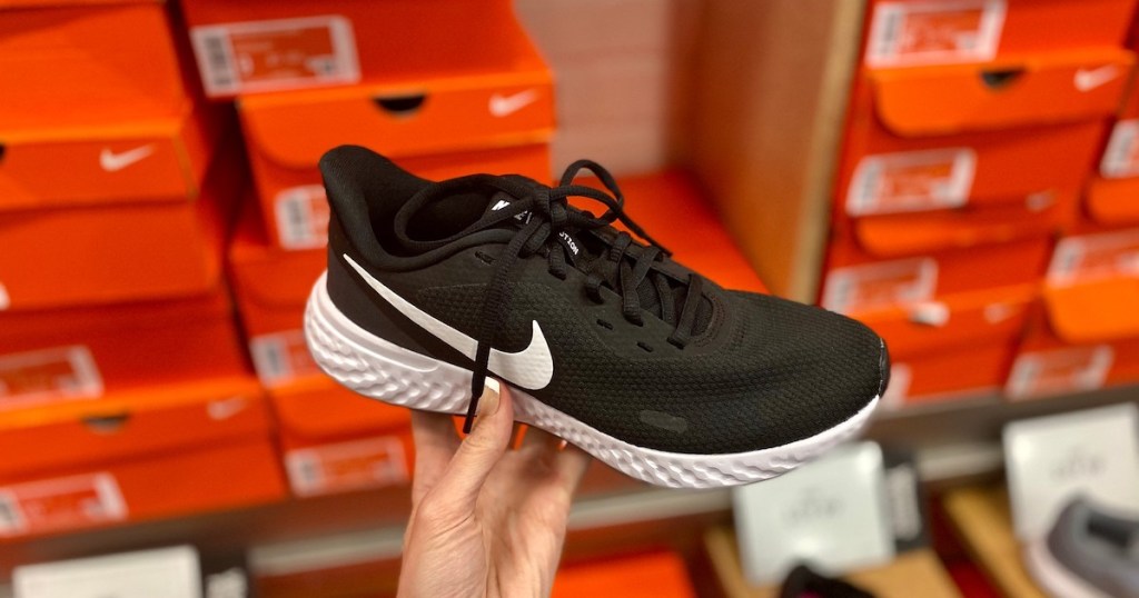 hand holding a black and white nike sneaker with orange nike boxes in the background