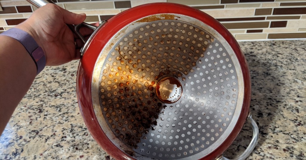 hand holding a red cooking pan with half clean half dirty bottom side