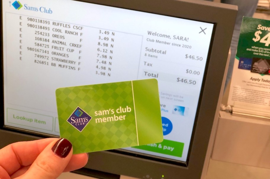 hand holding a green sam's club card in front of onlineputer screen with list of groceries and price