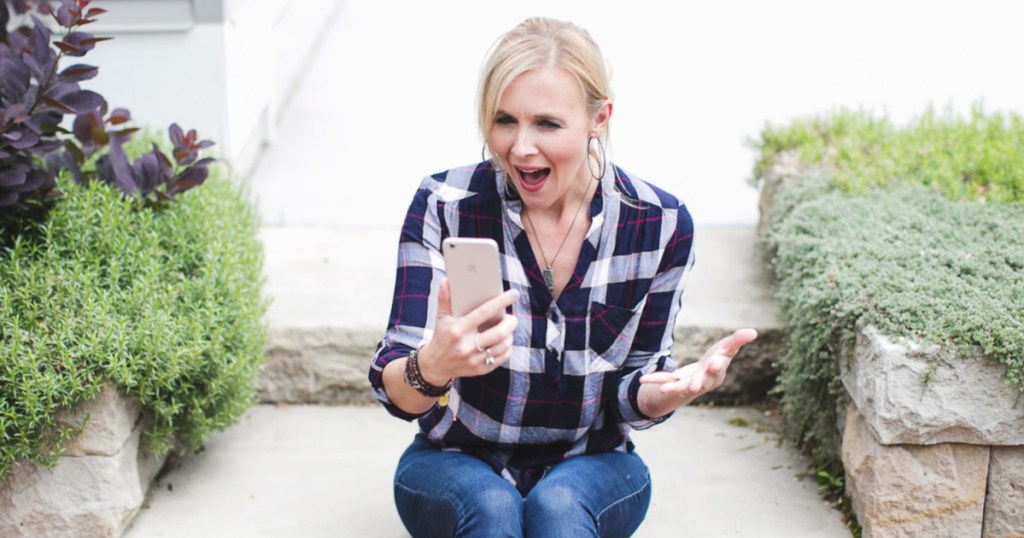 woman sitting on curb outside house using cell phone