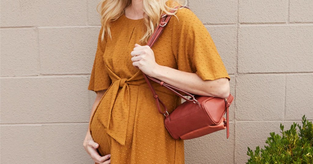 pregnant woman in yellow dress and red bag outside standing against wall