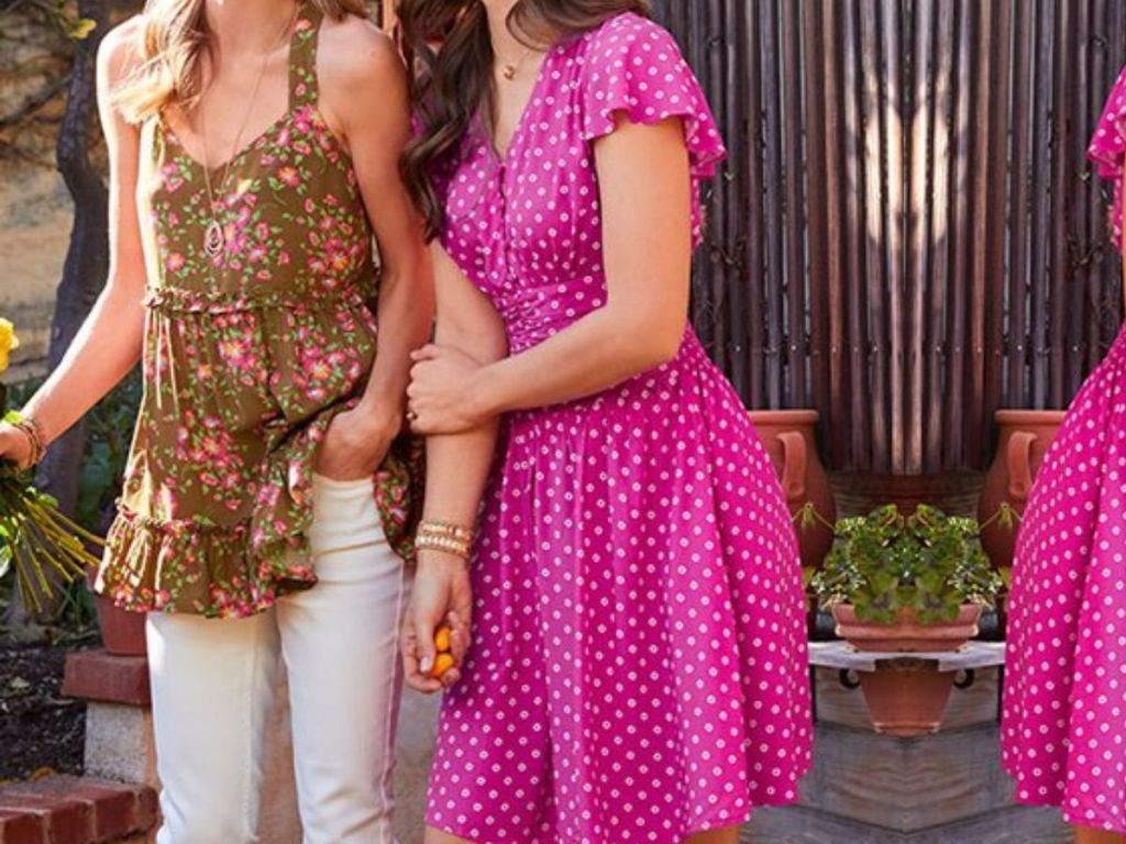 two women standing with arms interlocked wearing summer style clothing outside