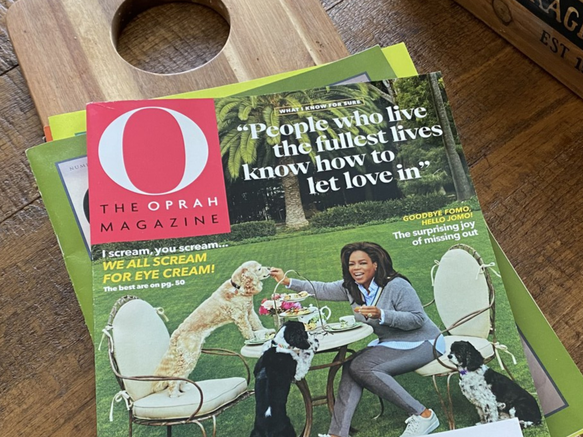 hand holding magazine in home above wood table and basket of potatoes