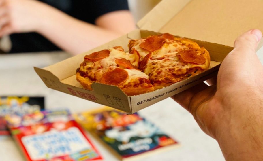 hand holding a personal pepperoni pizza in a box