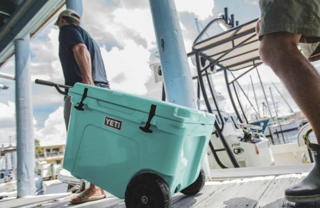 man pulling large teal wheeled cooler