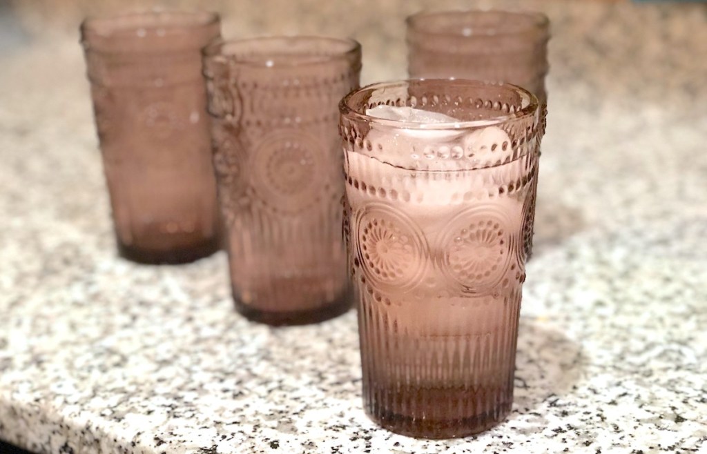 four purple pink drinking glasses sitting on granite countertop