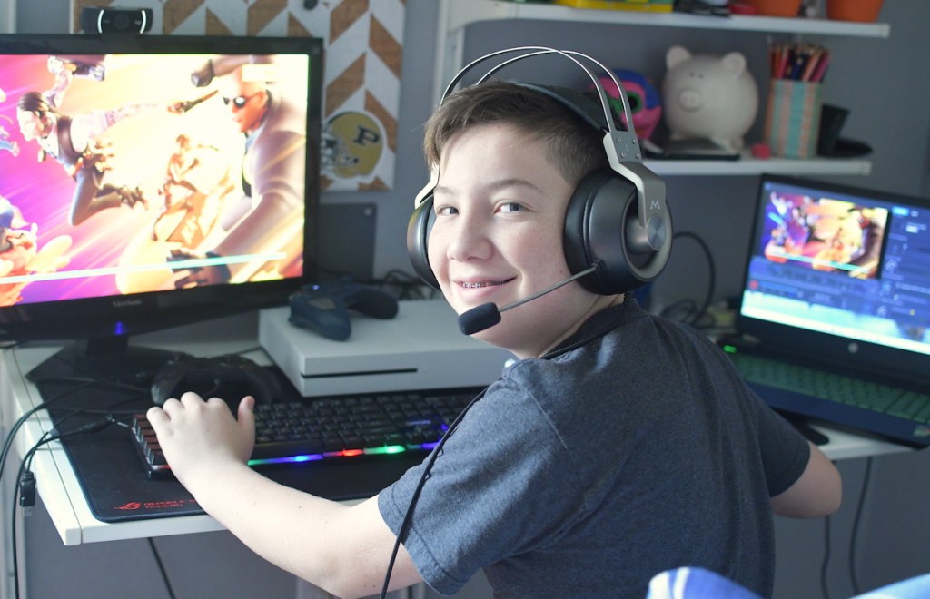 boy smiling wearing headphones sitting at desk with onlineputer gaming setup