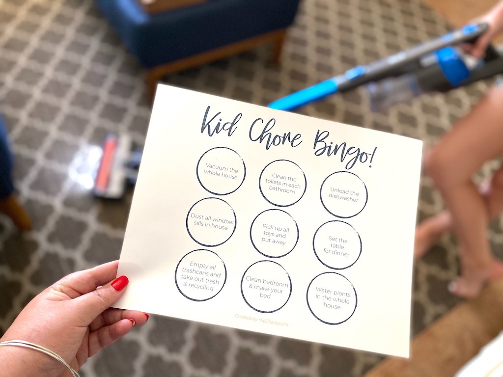 holding kid chore bingo printable with vacuum in background