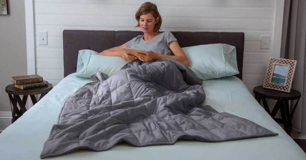 woman in bed reading a book with a weighted blanket on