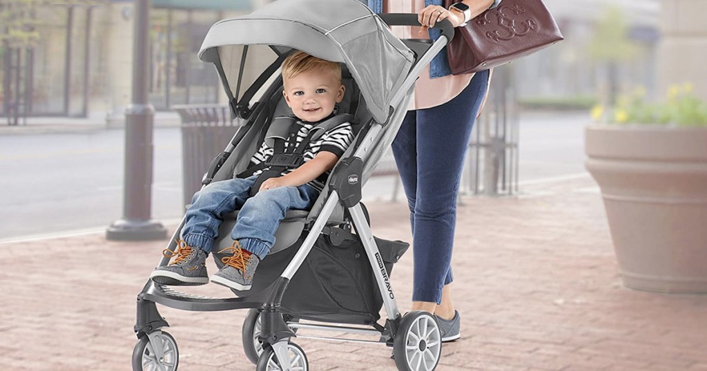 mother pushing child on sidewalk in grey and black baby stroller