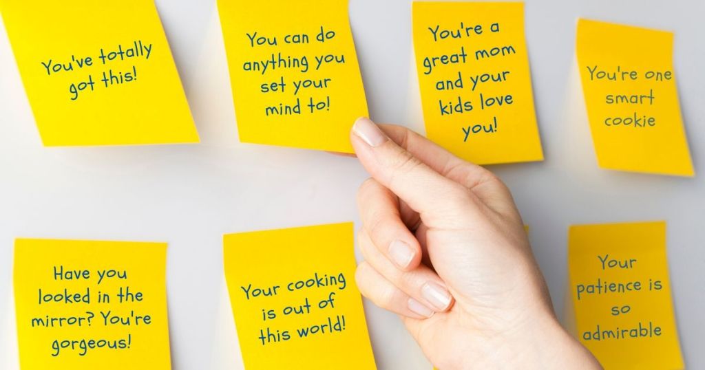 Hand grabbing an affirmation sticky note off the wall, next to other sticky notes